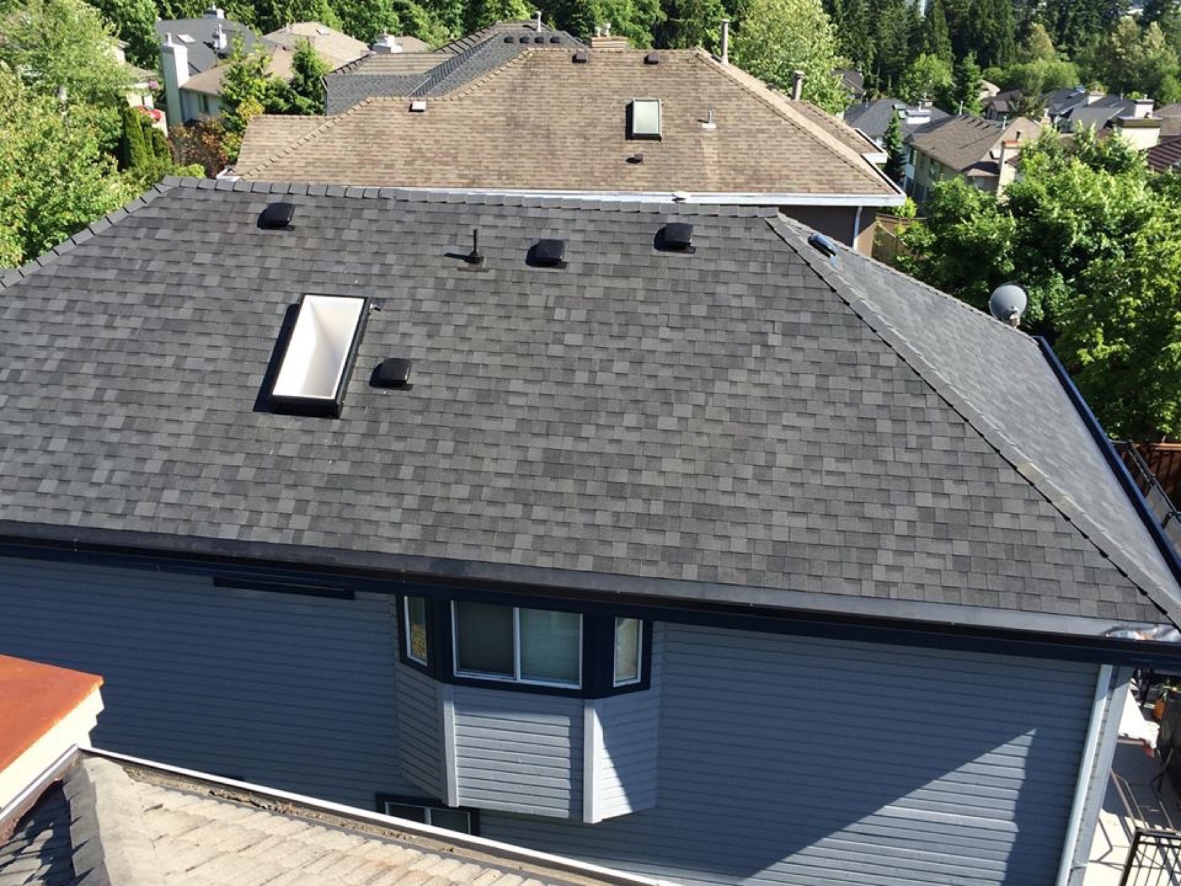 Completed grey shingle roof with skylights on a two storey house