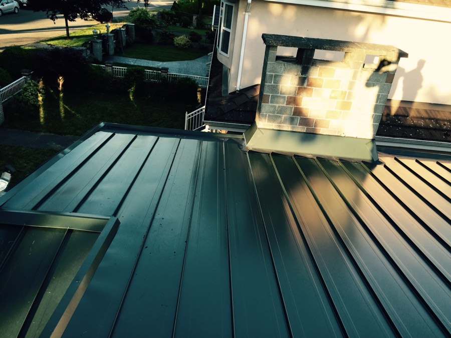 Green standing seam metal roof meeting a rendered chimney